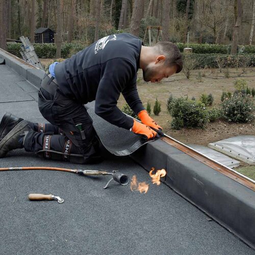 Dakbedekking specialist aan het werk op plat dak Dakdekker legt nieuwe waterdichte laag op plat dak in bosrijke omgeving.